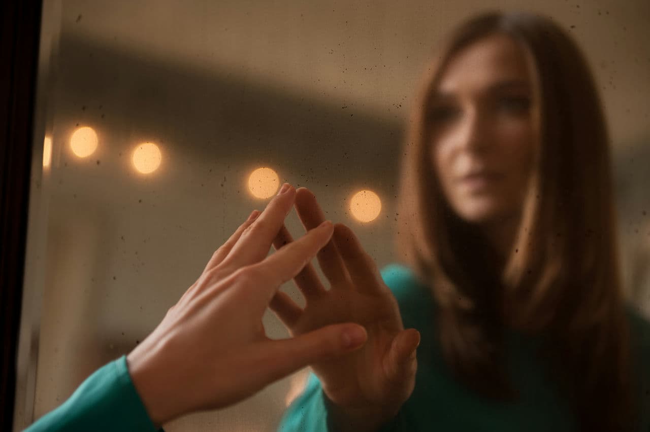 Young woman touching her own reflection in a vintage mirror