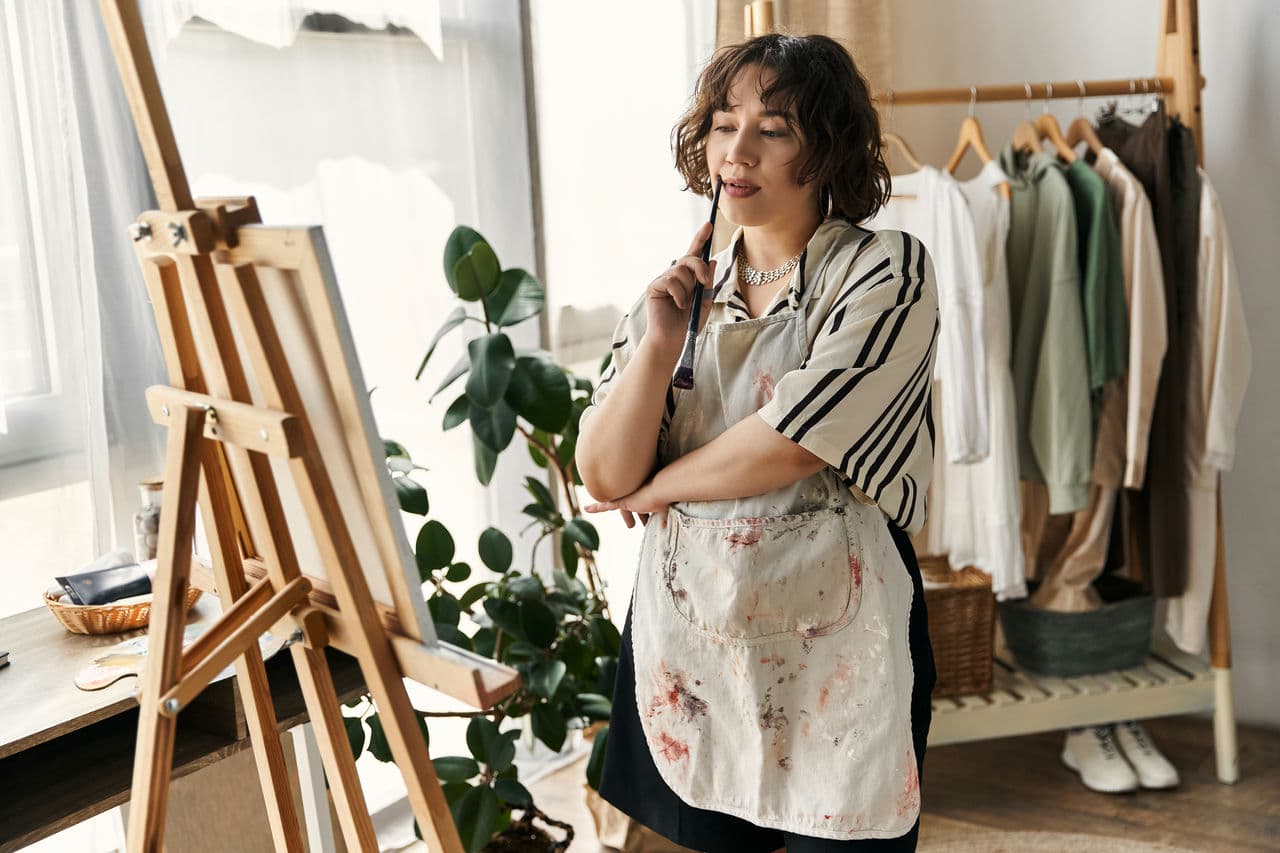 Curly-haired artist focuses on her canvas while surrounded by a modern apartment setup.