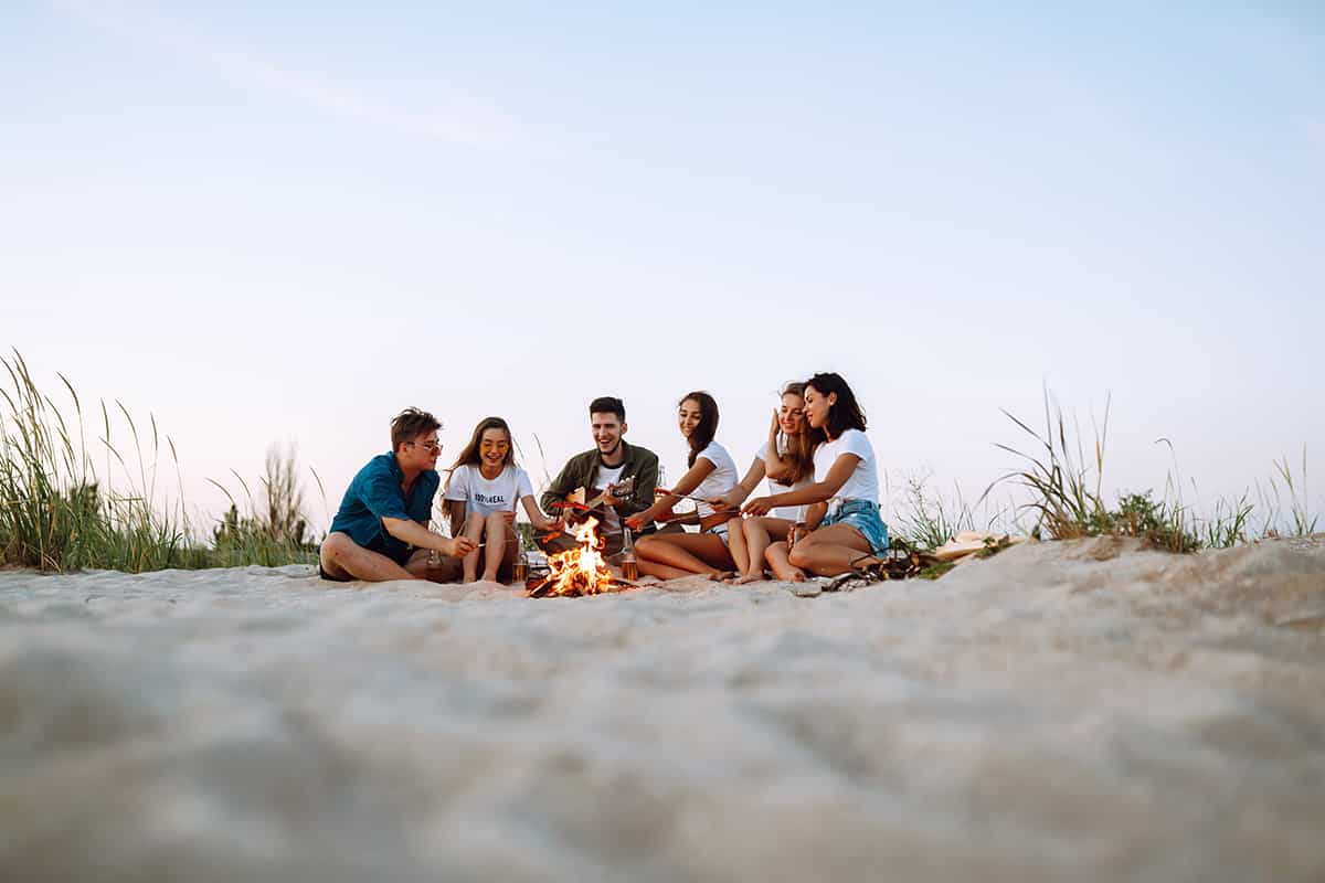 Group of smiling friends sitting by a campfire at the beach