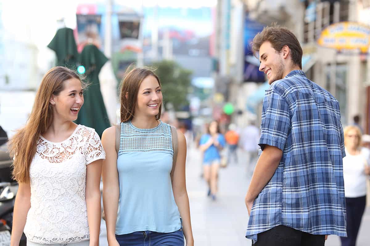 two women walking towards the camera and smiling at a passing man walking the opposite way who returns the smile