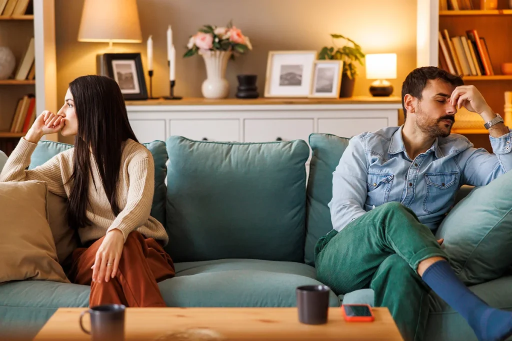 upset couple sitting i extreme ends of a couch ignoring each other